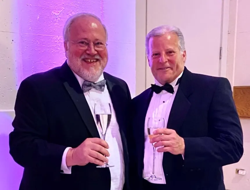 Two men is tuxedos holding up champagne glasses