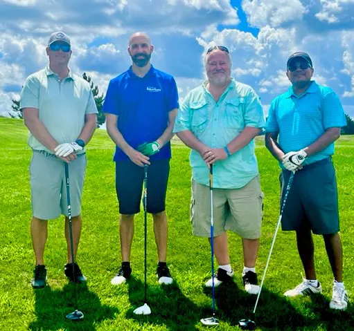 Four men holding golf clubs posing for photo on green grass in daylight