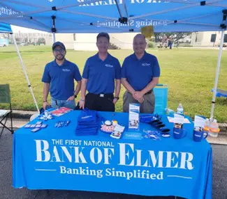 Three men standing behind table with Bank of Elmer banner hung