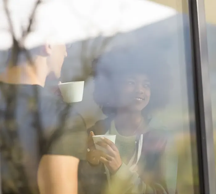 young couple drinking coffee behind house window