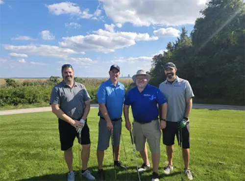 Group of men playing golf outside posing for photo with blue skies